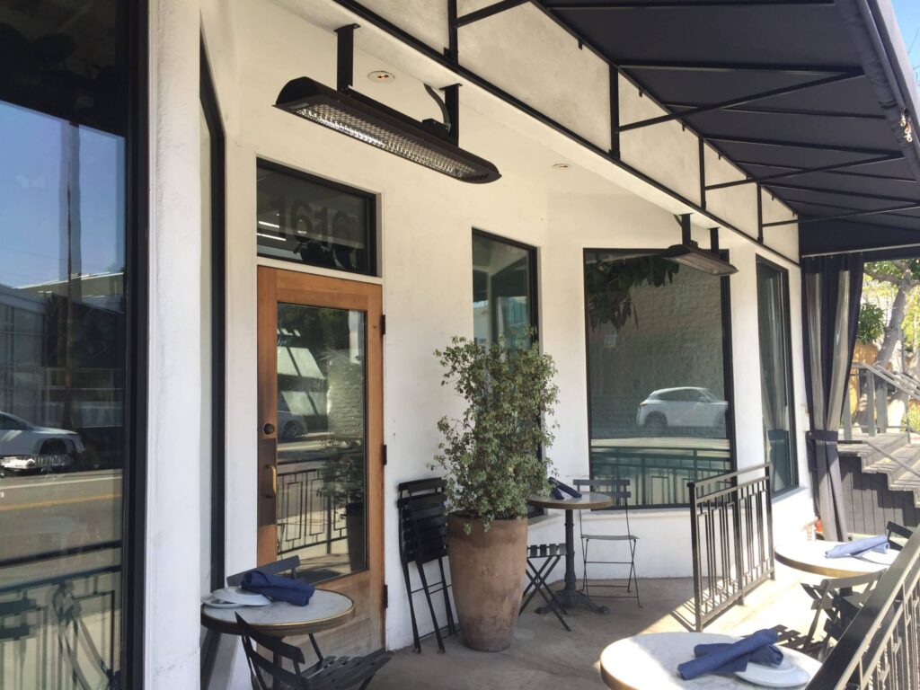 Cafe-Eingang mit kleinen Zweisitzertischen und Heizung über der Tür